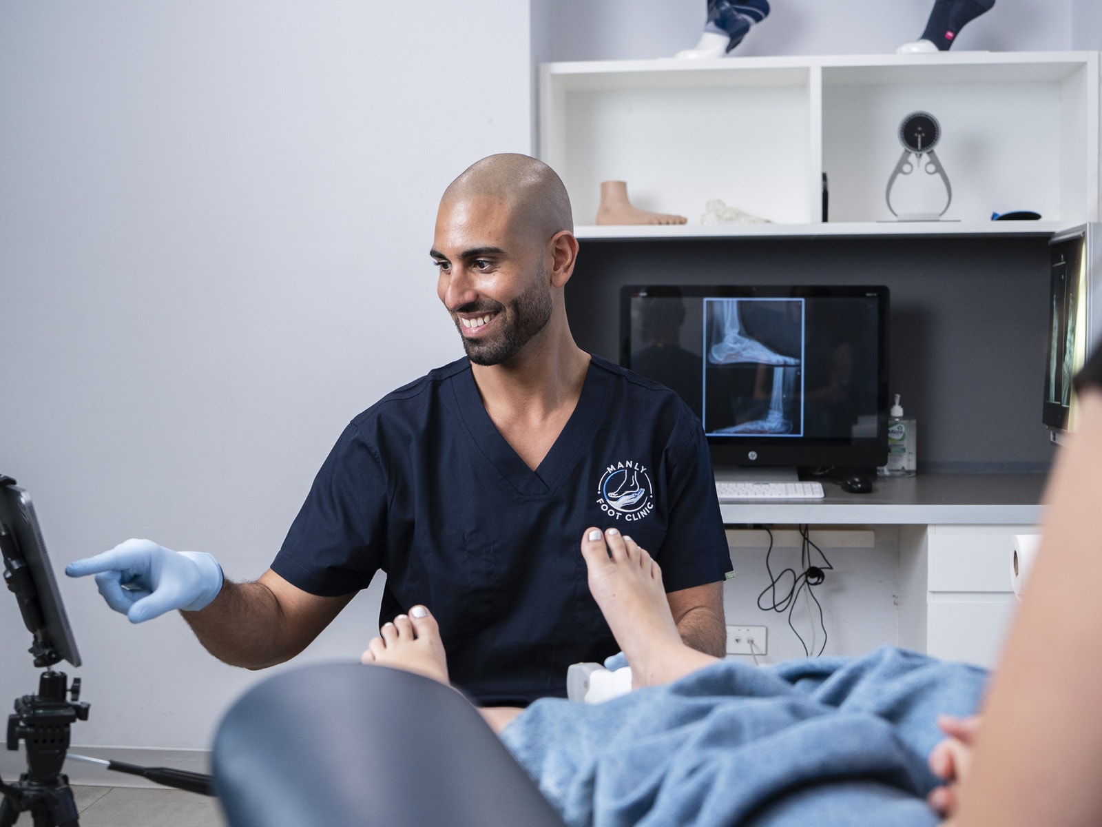 A podiatrist pointing to a screen during an assessment with a patient at Manly Foot Clinic