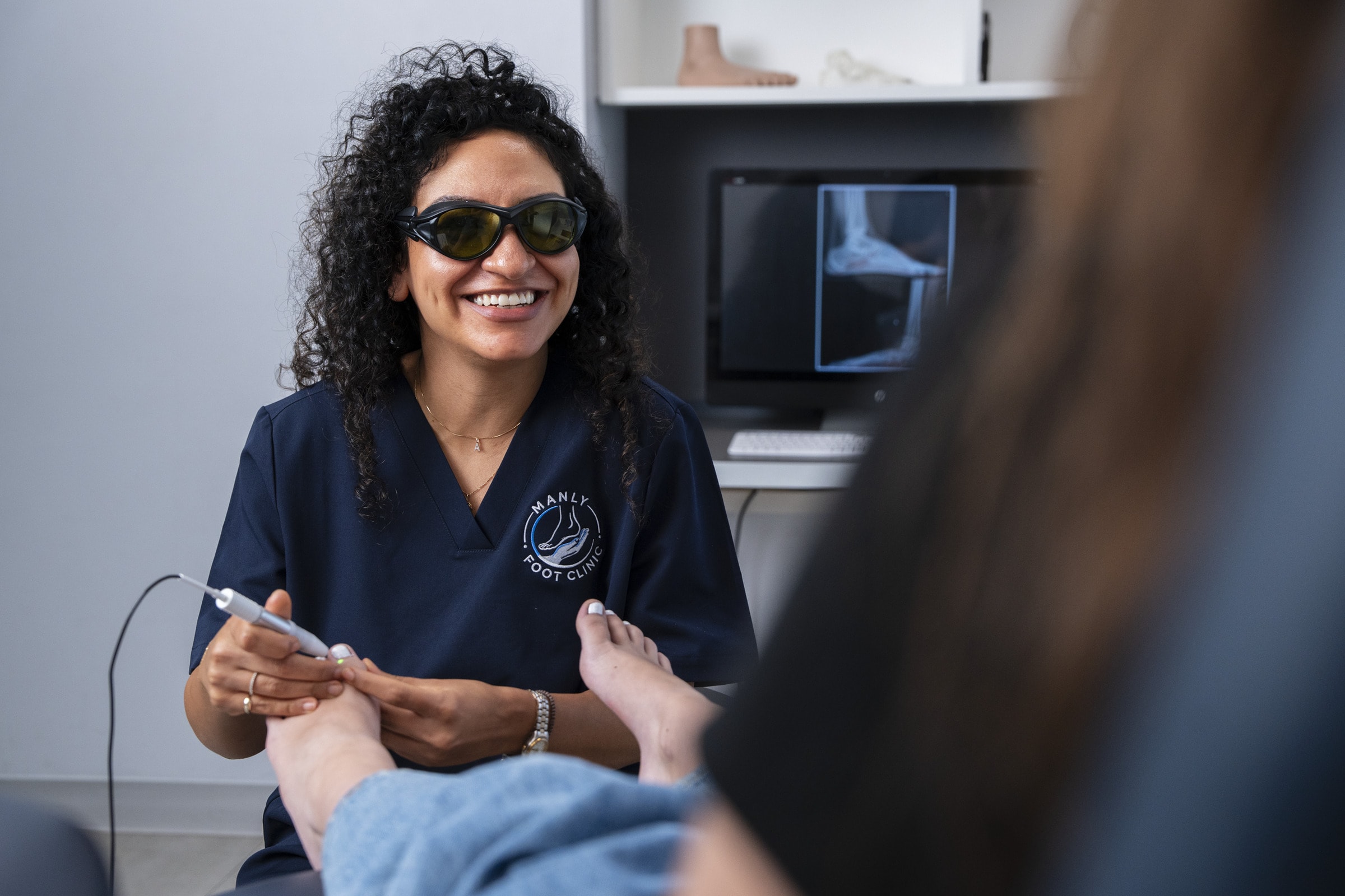 A podiatrist in protective glasses treating a patient’s toenail with a laser at Manly Foot Clinic