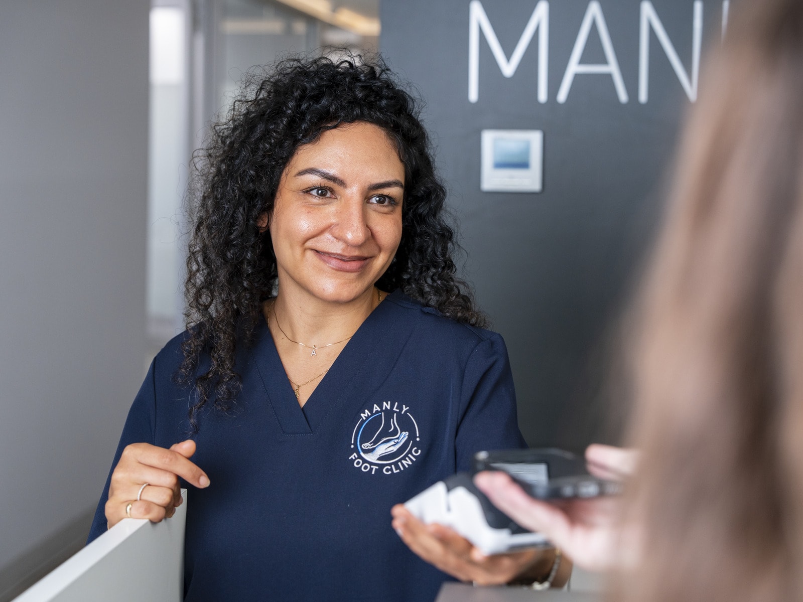 A podiatrist handing a patient their custom orthotics at the front desk of Manly Foot Clinic